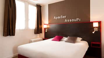 A hotel room with a large bed, brown curtains, a wall-mounted sign reading "Aposer AssouPI", and two bedside lamps.