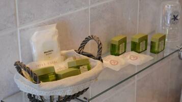 A bathroom with a glass shelf displaying toiletries and a basket with a bag labeled "INTER-HOTEL" and green soap bars.