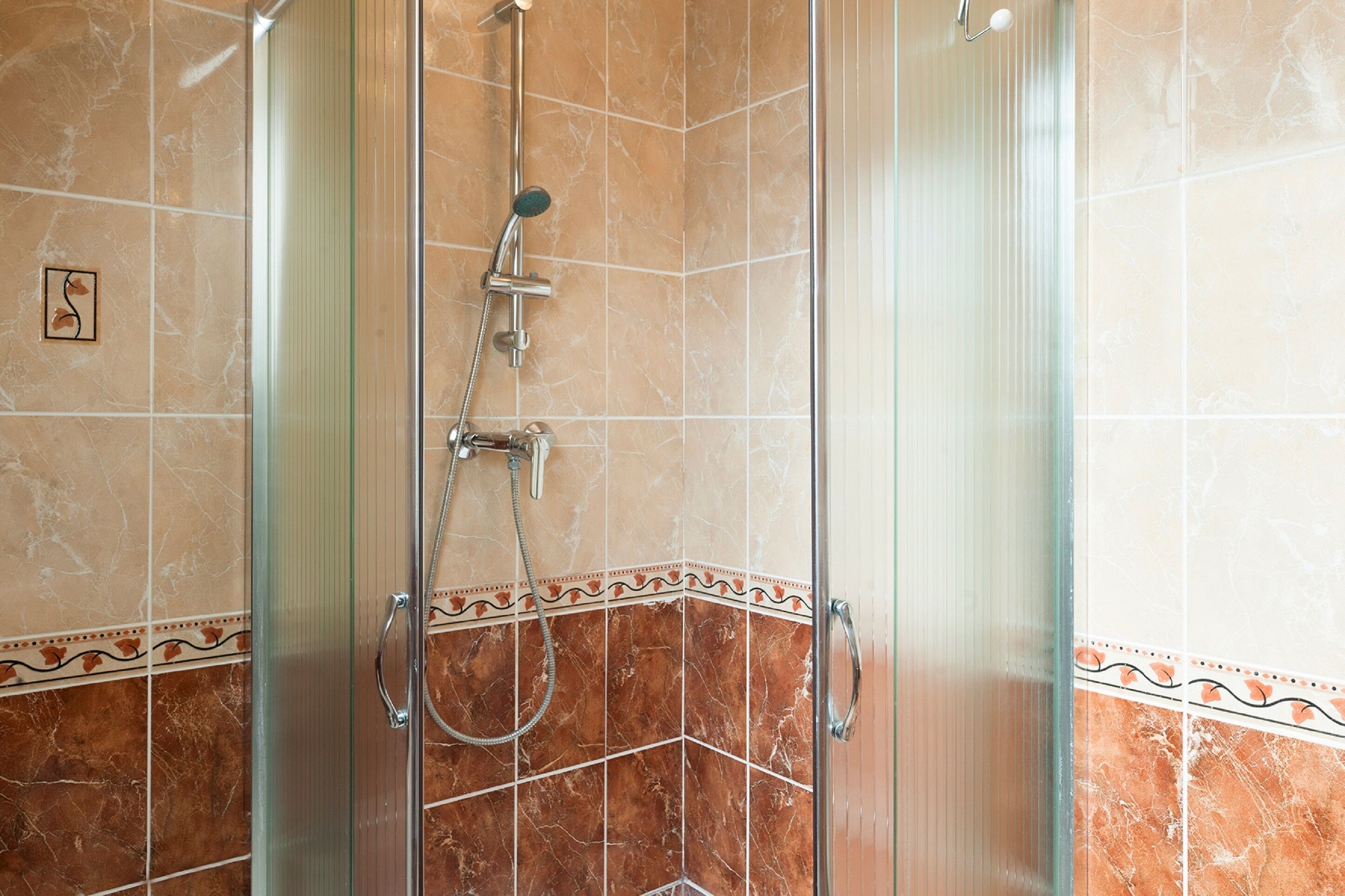 A glass-enclosed shower with a handheld showerhead and a wall-mounted faucet.