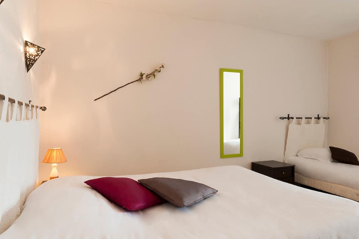 Ett välordnat hotellrum med en säng, ett sängbord, en lampa och en spegel som är monterad på väggen.