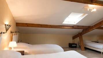 A cozy attic bedroom with two beds, a skylight, wooden beams, and a small bedside table with a lamp.