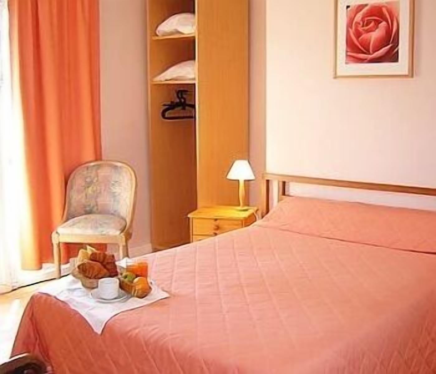 Habitació d'hotel amb un llit, una cadira, una tauleta de nit amb una làmpada i un quadre a la paret.