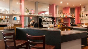 A bar area with a counter, stools, and shelves with bottles and glasses.