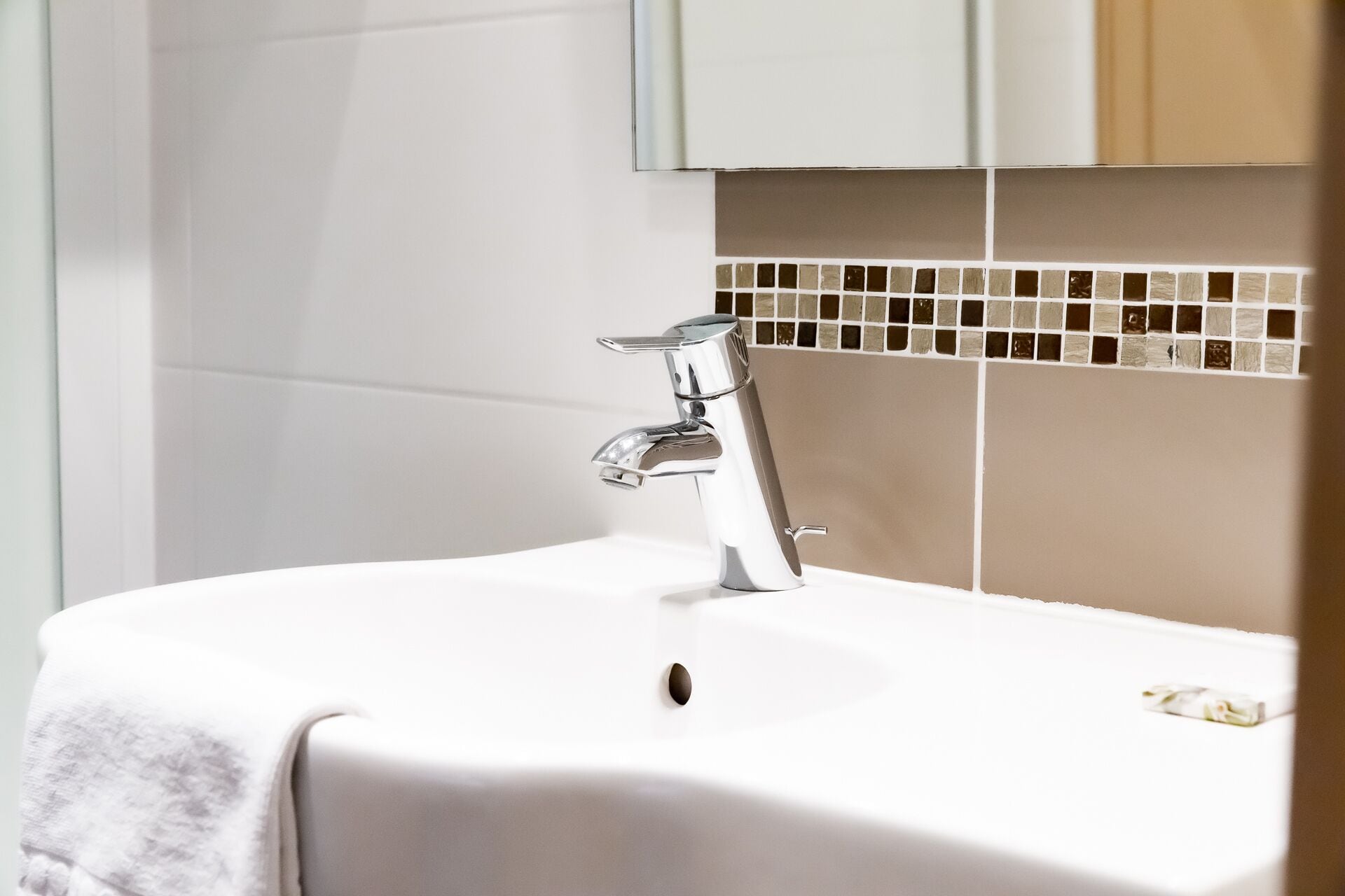 Une salle de bain avec un lavabo blanc, un robinet chromé et un mur recouvert de carreaux.