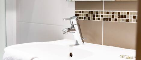 Une salle de bain avec un lavabo blanc, un robinet chromé et un mur recouvert de carreaux.
