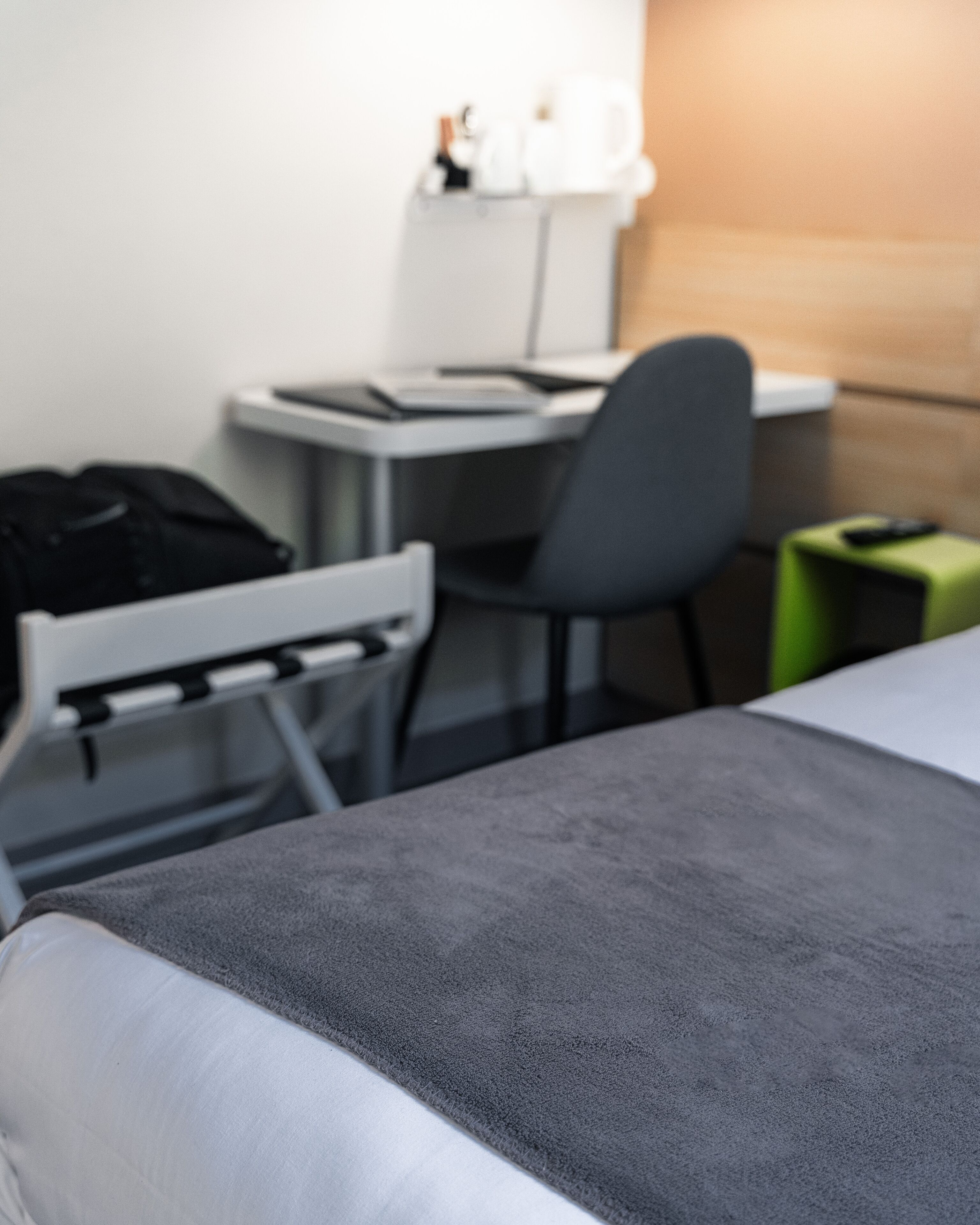 Een hotelkamer met een bed, een bureau, een stoel en een klein groen krukje.