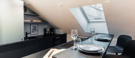 A modern kitchen with a dining area, featuring a skylight, dark cabinetry, and a clean, minimalist design.