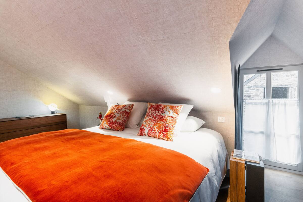 Un dormitorio con una cama grande, una mesita de noche de madera, una ventana con cortinas y vistas al exterior.