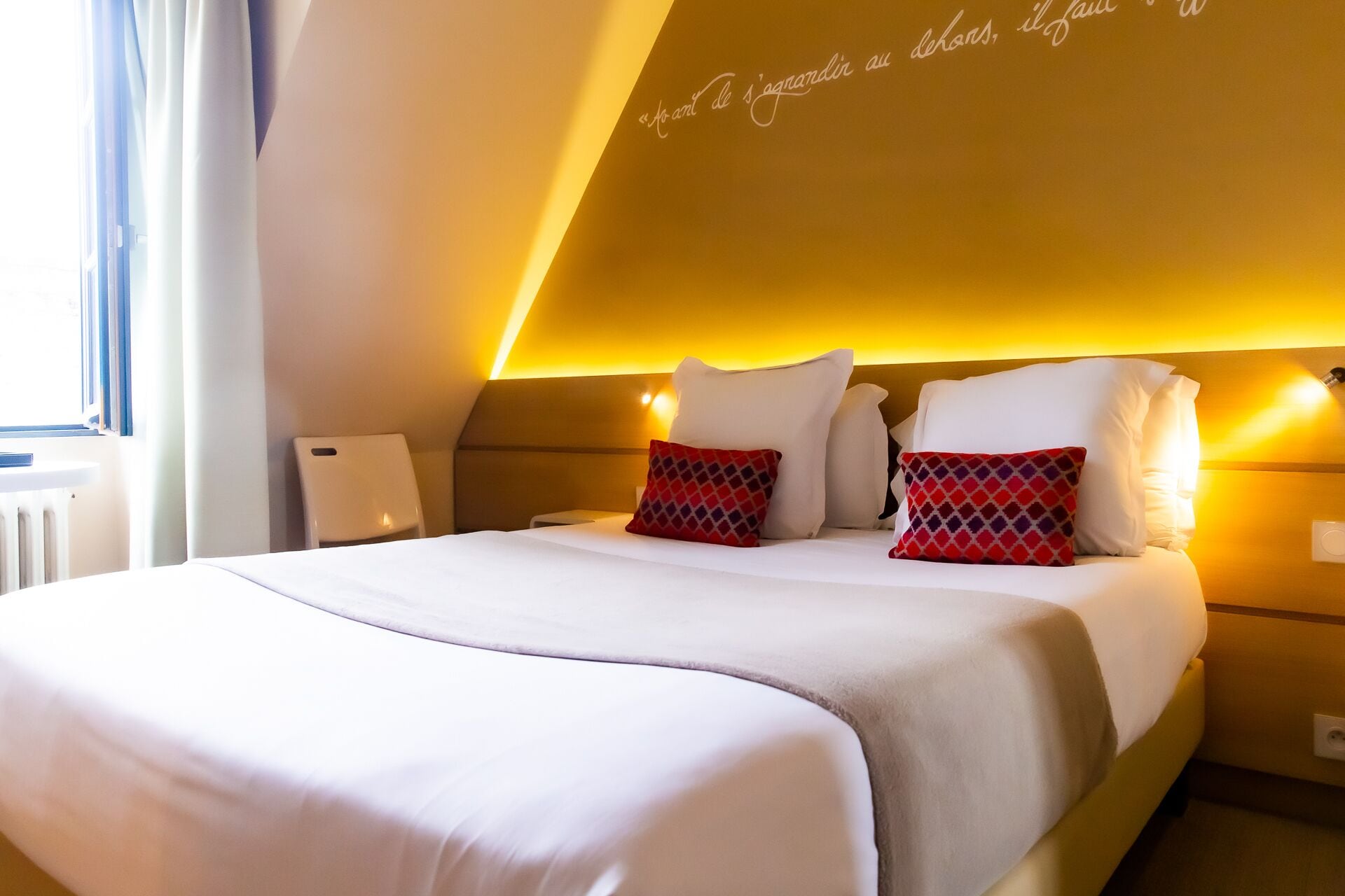 A modern hotel room with a large bed, two pillows, and a bedside table.