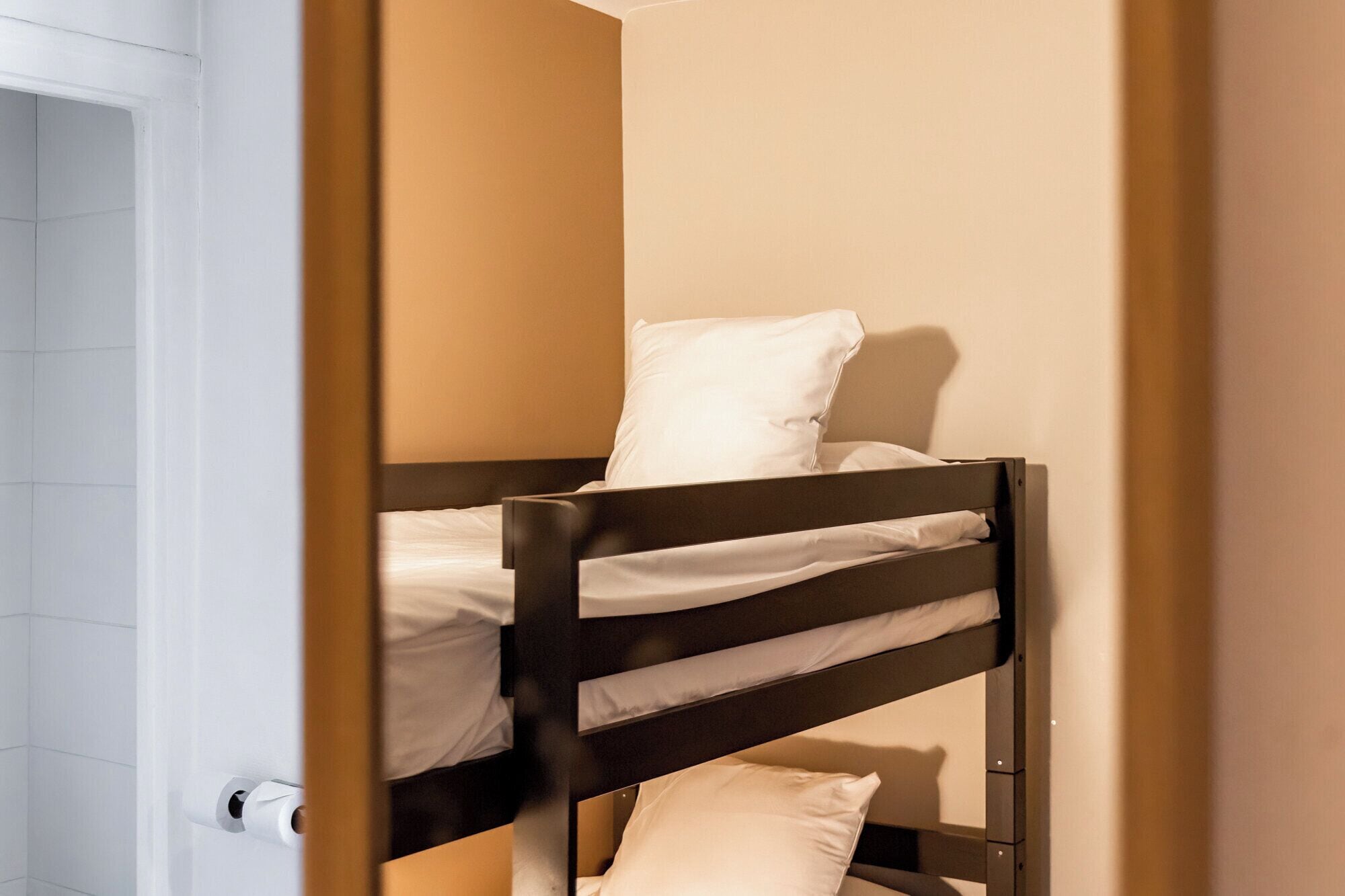 A bunk bed with white bedding in a room with beige walls.