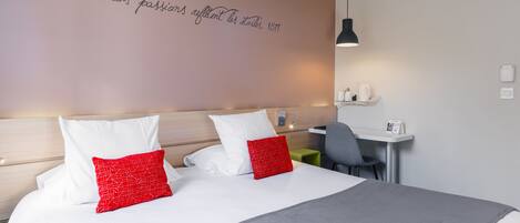 A neatly made bed with white and red pillows, a grey blanket, and a wall with a motivational quote.