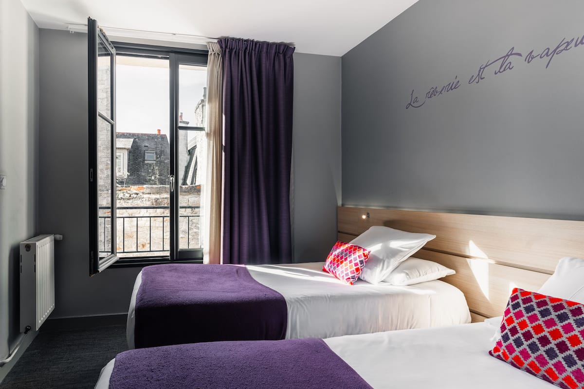 Habitación de hotel con dos camas, un ventanal grande y vistas a edificios.