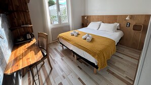 Hotelkamer met een bed, houten hoofdbord, nachtlampjes, een raam met gordijnen, een houten bureau met waterkoker en uitzicht op de omgeving.