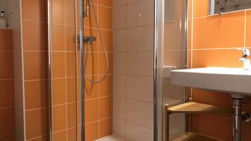 Una ducha con puerta de cristal, un lavabo blanco y paredes con azulejos naranjas.