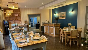 Een eetruimte met een houten tafel voor vier personen, omringd door rieten stoelen. Achtergrond toont een keuken met een koelkast en een magnetron.