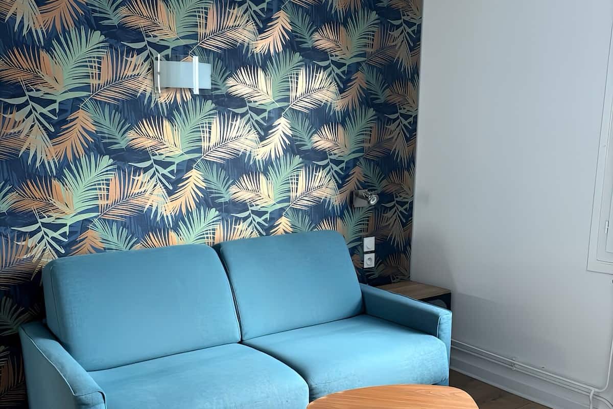 A modern living room with a blue sofa, a wooden coffee table, and a patterned wall.