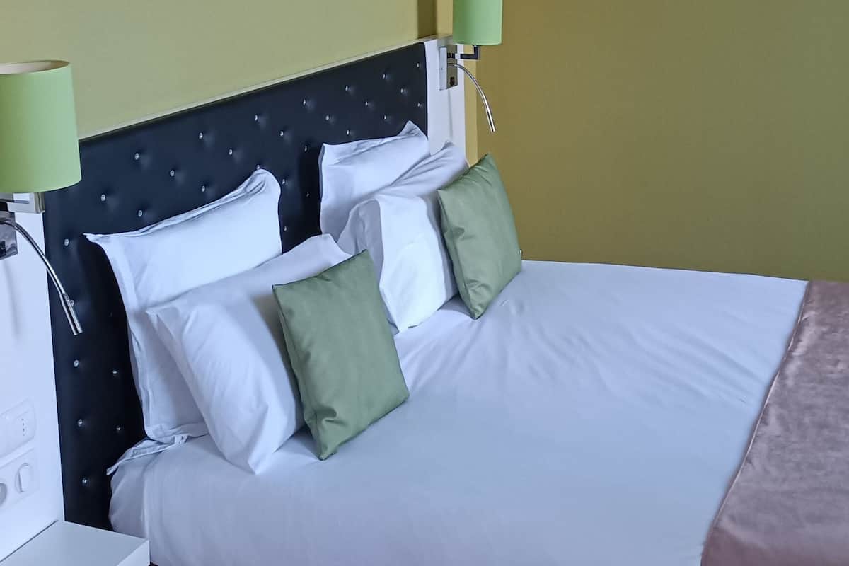 Ein Hotelzimmer mit einem Bett, grünen Kissen, einem Kopfteil, einem Wandbild einer Frösch und zwei Nachttischlampen.