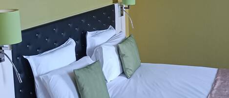 A hotel room with a bed, green pillows, a headboard, a wall painting of a frog, and two bedside lamps.