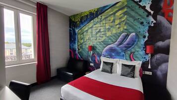 Ein Hotelzimmer mit einem großen Bett, einem Sessel, einem Fenster mit Vorhängen und einem farbenfrohen Wandgemälde.