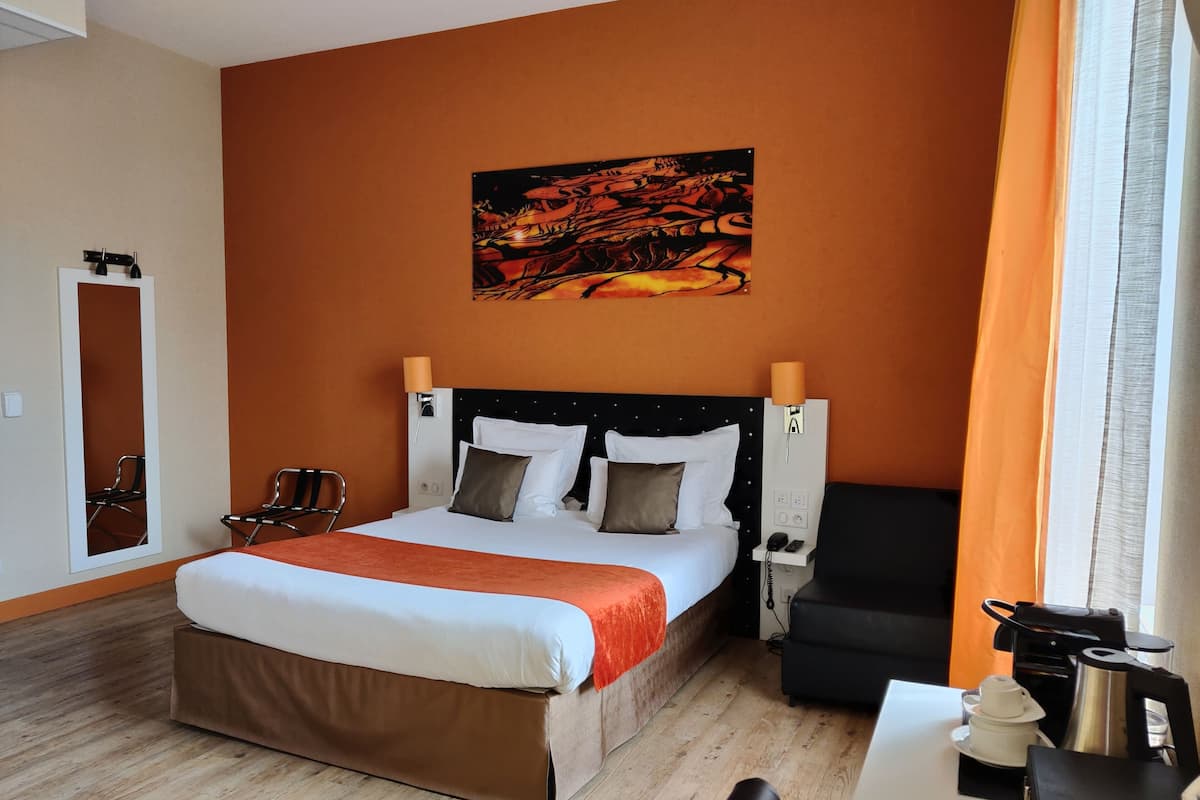 Ein Hotelzimmer mit Bett, Schreibtisch, Stuhl, einer Kaffeemaschine und einem Bild an der Wand.
