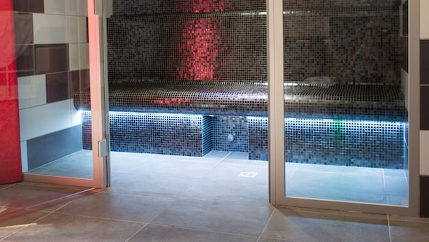 A modern bathroom with a glass shower enclosure, tiled walls, and a visible bench.
