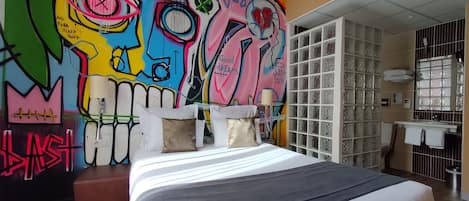 A bedroom with a colorful graffiti mural on the wall, a bed with white and gray bedding, and a small wooden bench.