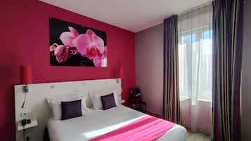 Habitación de hotel con una cama grande, una pared roja, un cuadro de flores rosas y una ventana con cortinas a rayas.