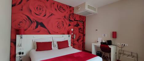 A hotel room with a large bed, a desk, and a red rose wallpaper.