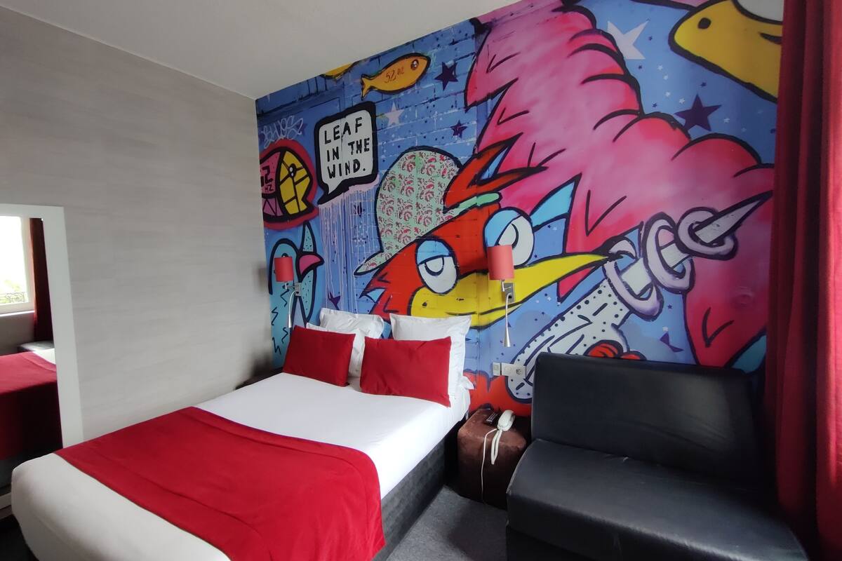 Ein Hotelzimmer mit einem Bett, einer roten und weißen Farbgestaltung, einem Wandgemälde und einem roten Vorhang.