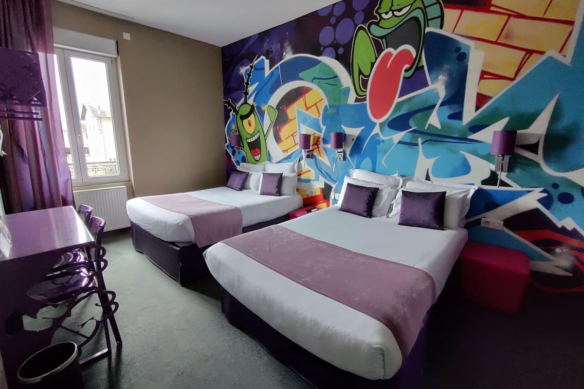Ein Hotelzimmer mit zwei Betten, einem Schreibtisch und einer Wand mit bunten Graffiti.