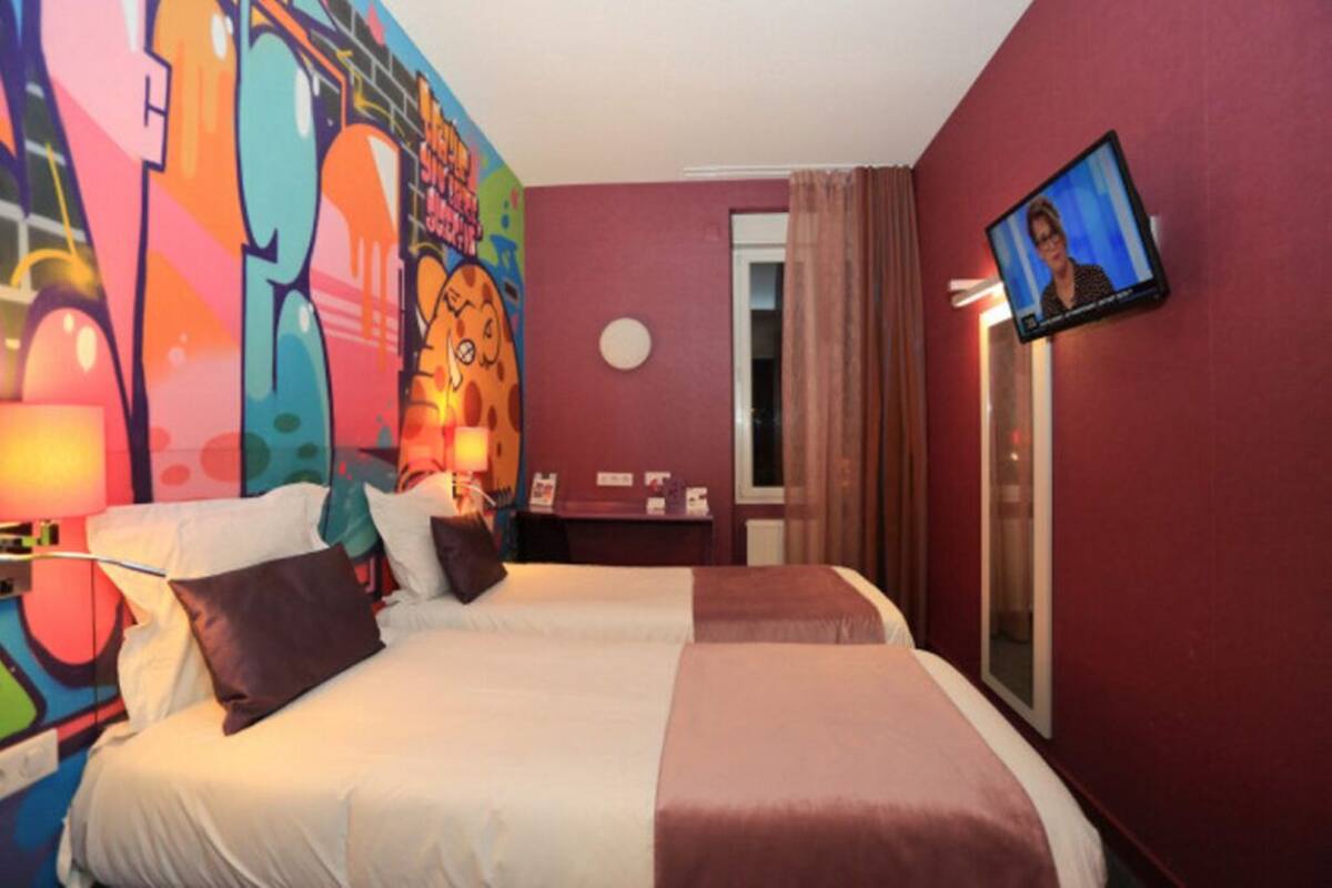 Ein Hotelzimmer mit zwei Betten, einem an der Wand montierten Fernseher und einem farbenfrohen Wandgemälde.