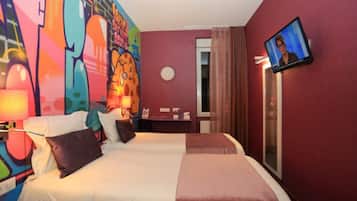 Habitación de hotel con dos camas, un televisor montado en la pared y un mural colorido.