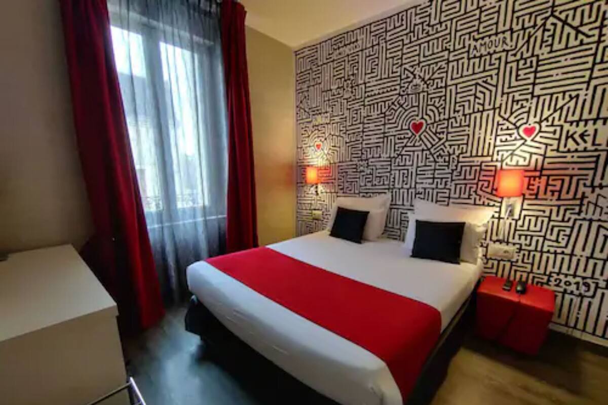 Ein Hotelzimmer mit einem großen Bett, roten Vorhängen, einer Wand mit Muster und zwei Nachttischlampen.