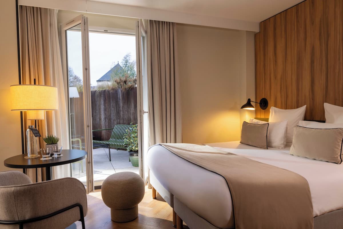 A hotel room with a bed, bedside tables, a lamp, a chair, and a view of the outside.