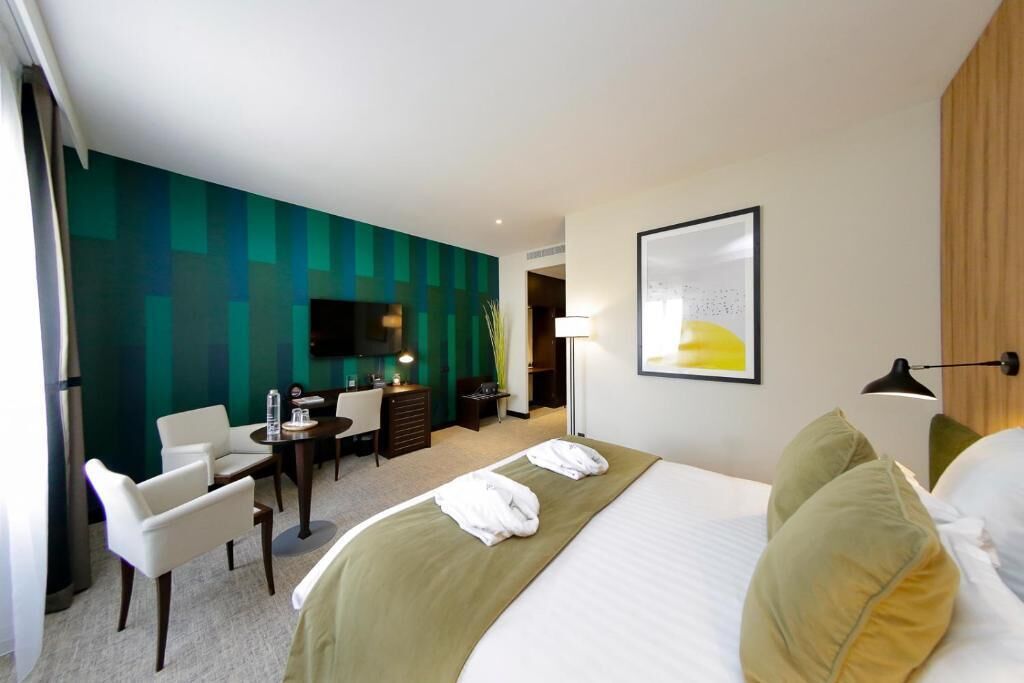 A hotel room with a bed, a desk, a chair, and a TV.