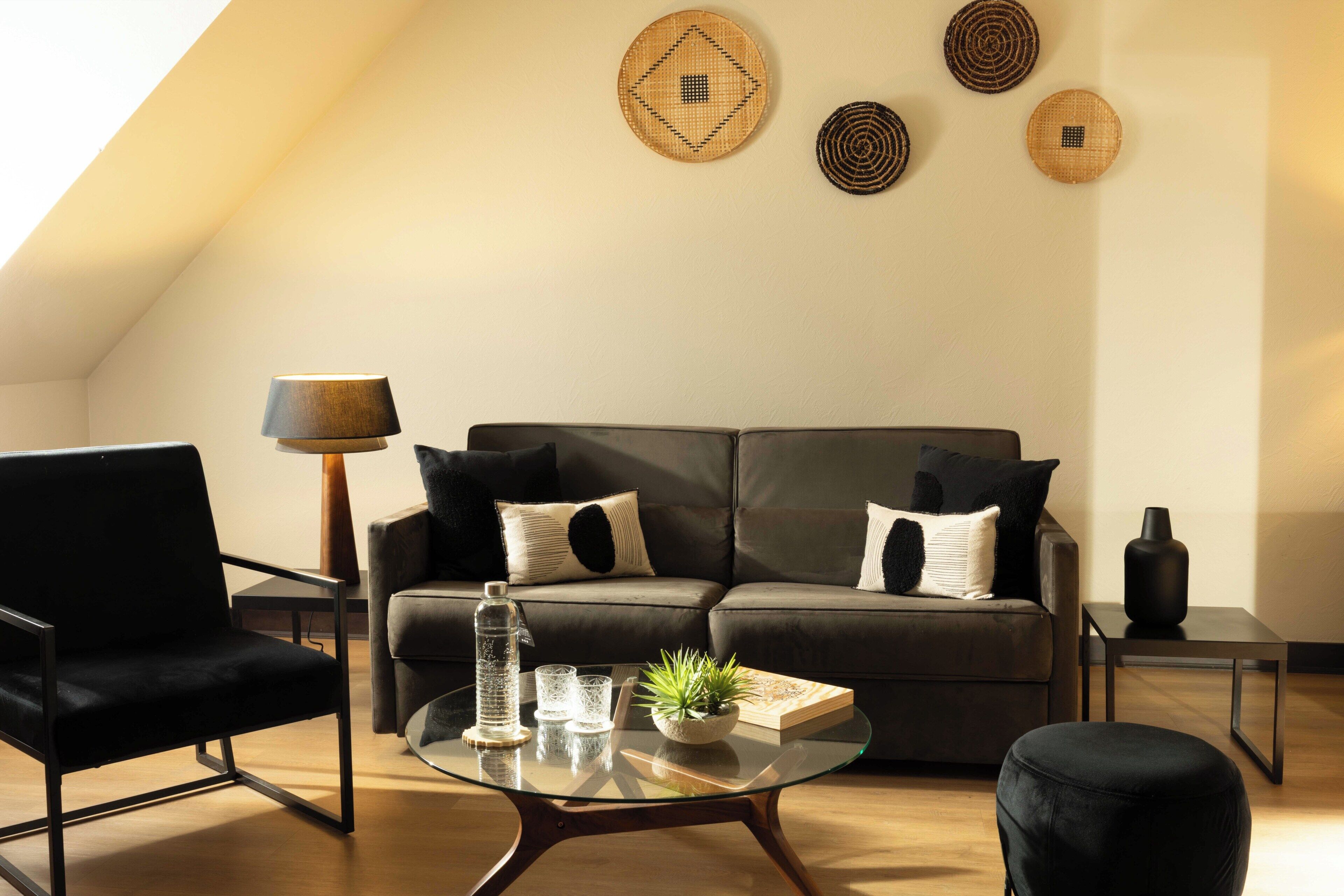 Un salon moderne avec un canapé, une table basse en verre, une lampe sur pied et des œuvres d’art décoratives accrochées au mur.