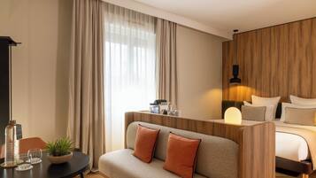 Habitación de hotel con sofá, cama, un muro decorativo de madera, lámpara y una pequeña mesa con planta y vasos.