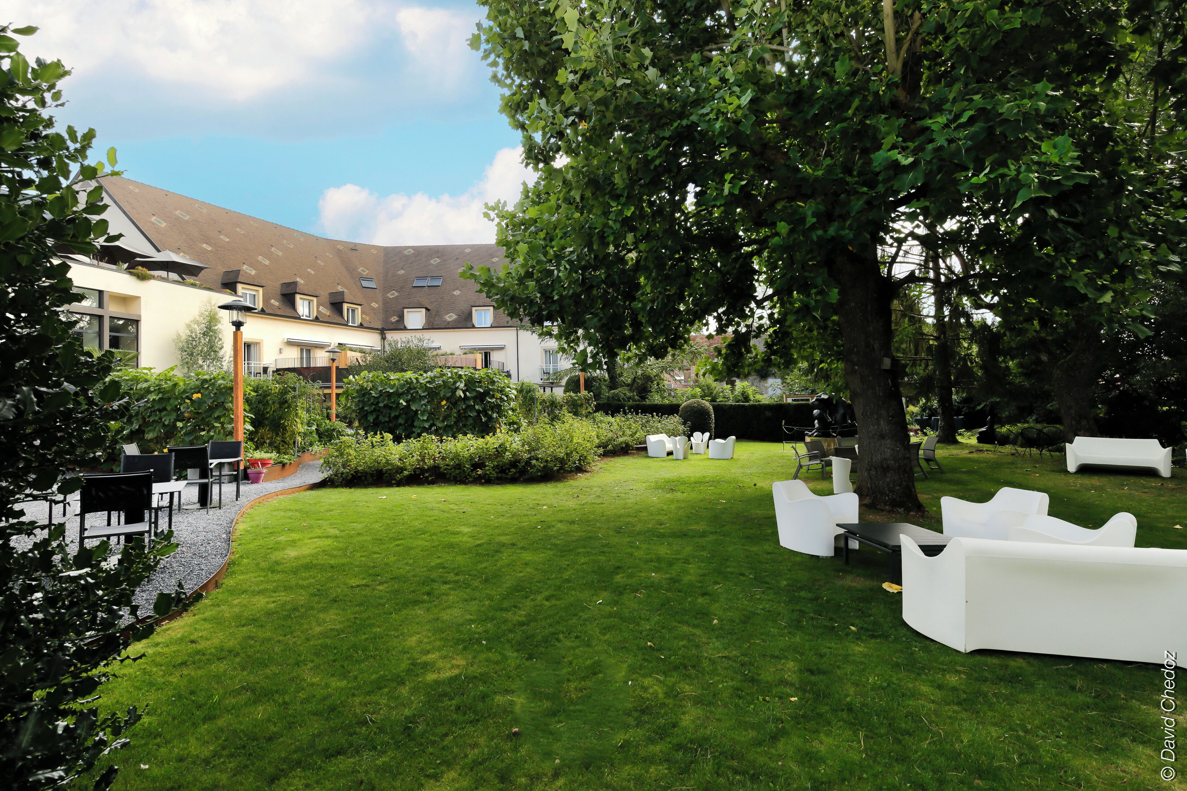 Un espace extérieur bien entretenu, avec des meubles de jardin blancs, une pelouse verdoyante et un bâtiment doté de nombreuses fenêtres et d’un toit en pente.