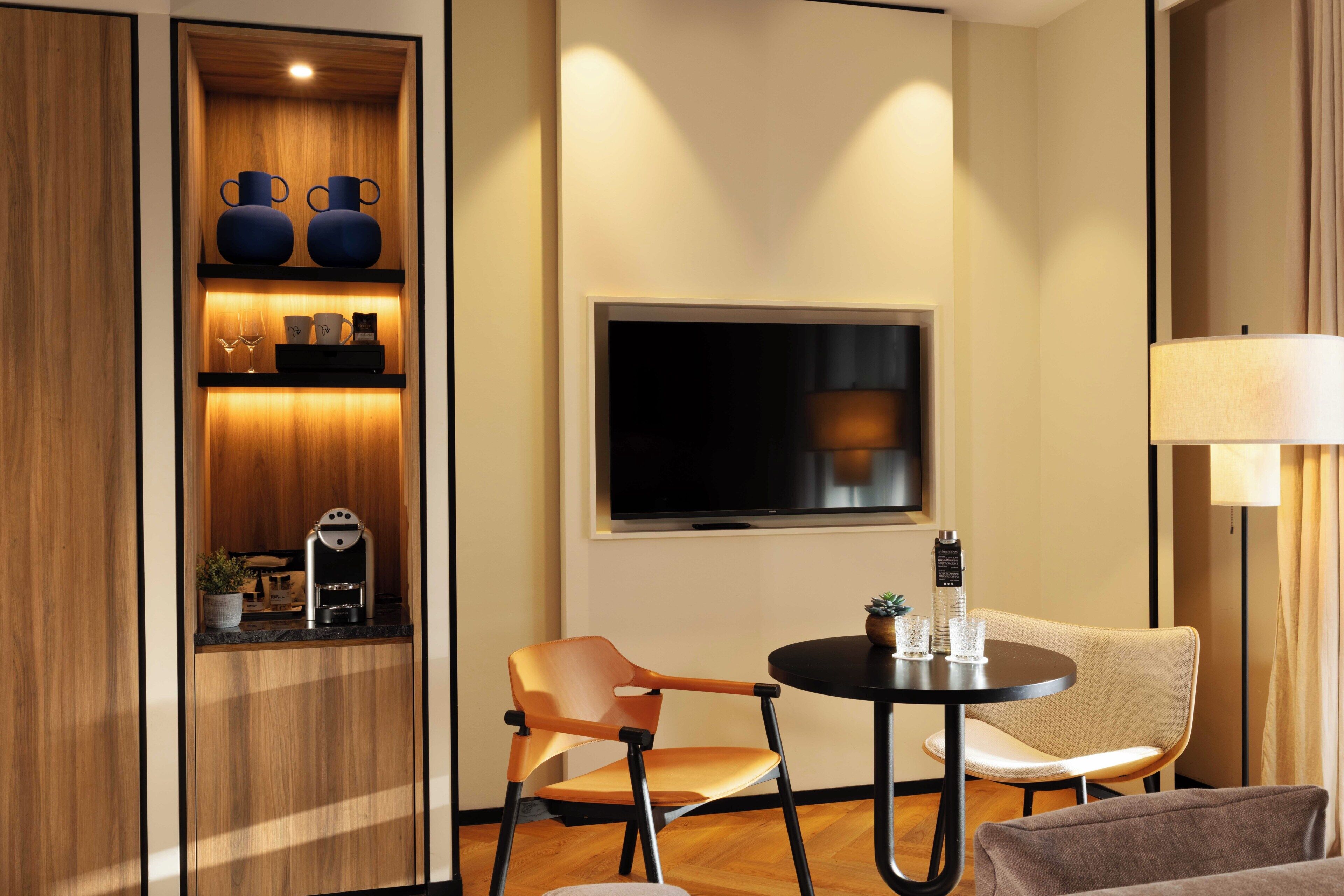 Ein modernes Zimmer mit einem Holzkorpus, einem Fernseher, einem runden Tisch mit zwei Stühlen und einer Lampe.