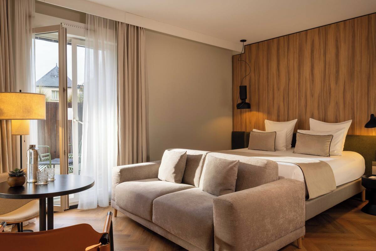 A hotel room with a bed, a sofa, a table, and a lamp.