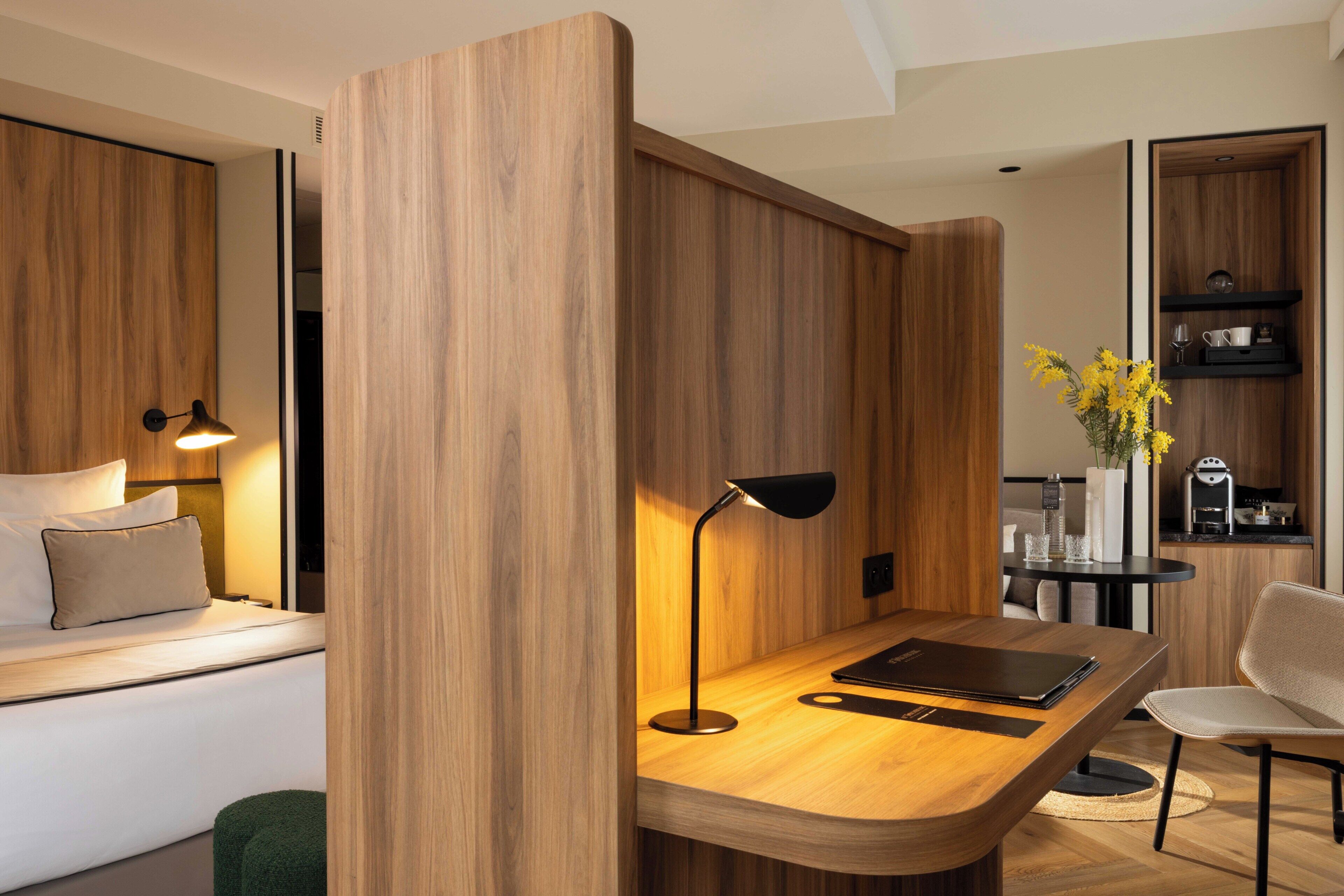 Una habitación de hotel moderna con una pared de madera decorativa, un escritorio con lámpara, una silla y una pequeña mesa con un jarrón de flores.