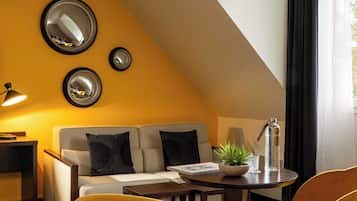 Una habitación moderna con sofá, un sillón amarillo, una mesa redonda con una planta y una botella de agua, y tres espejos montados en la pared.