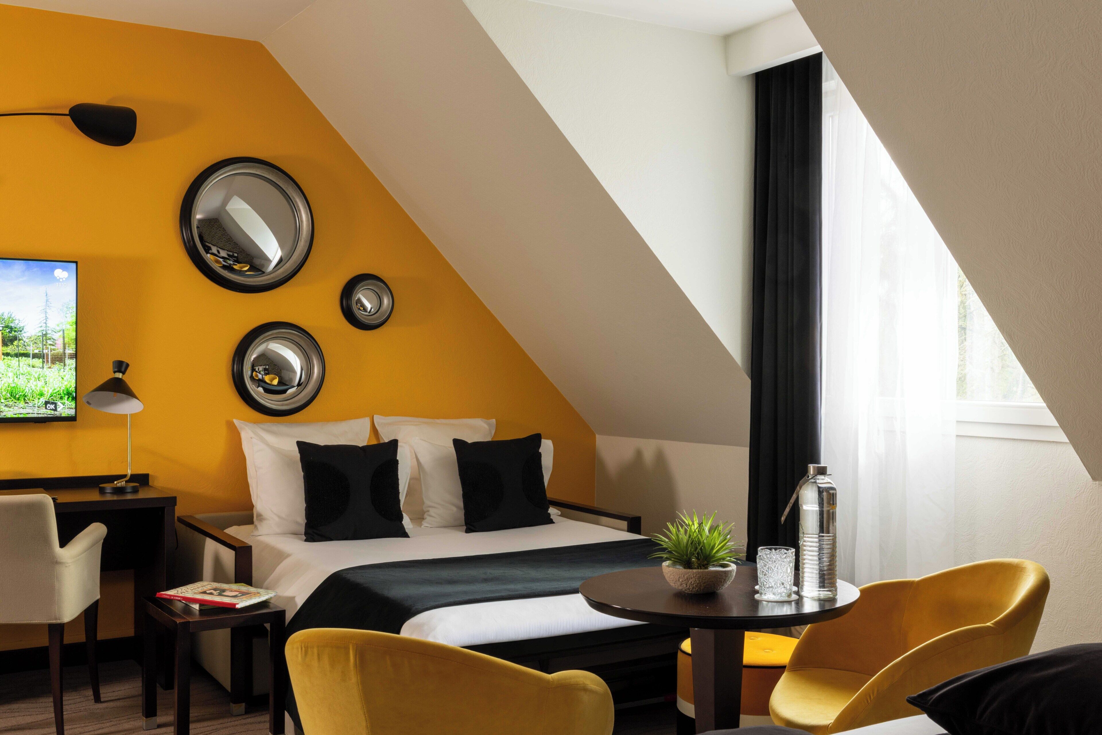 Habitación de hotel con cama, escritorio, silla, mesa con planta y ventana con cortinas.