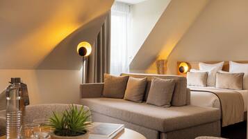 A modern hotel room with a sofa, a bedside table with a plant, a lamp, and a bed with pillows.