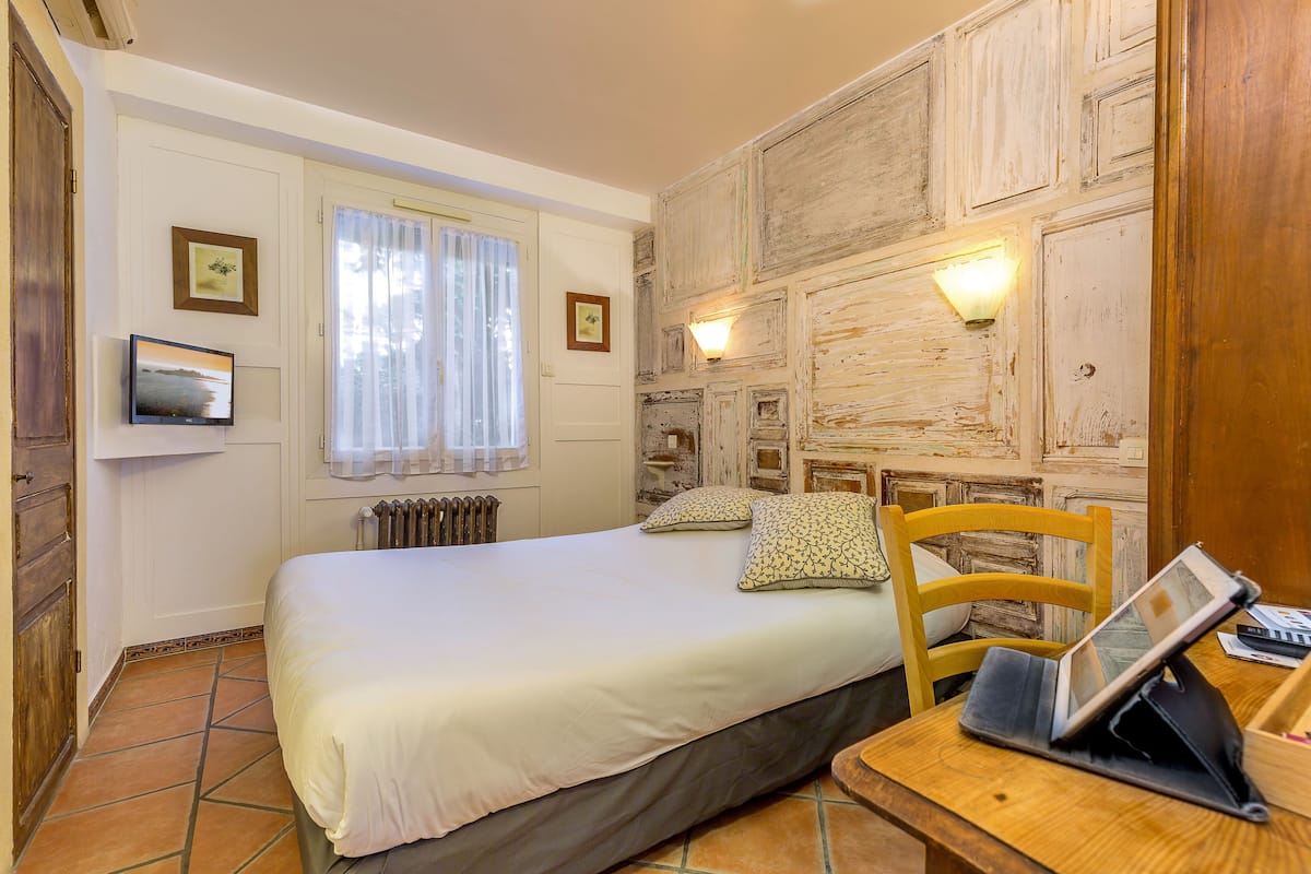 Une chambre à coucher comprenant un lit, une chaise en bois, une table de chevet avec une tablette et deux lampes fixées au mur.