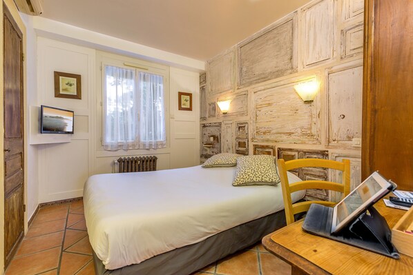 Une chambre à coucher comprenant un lit, une chaise en bois, une table de chevet avec une tablette et deux lampes fixées au mur.