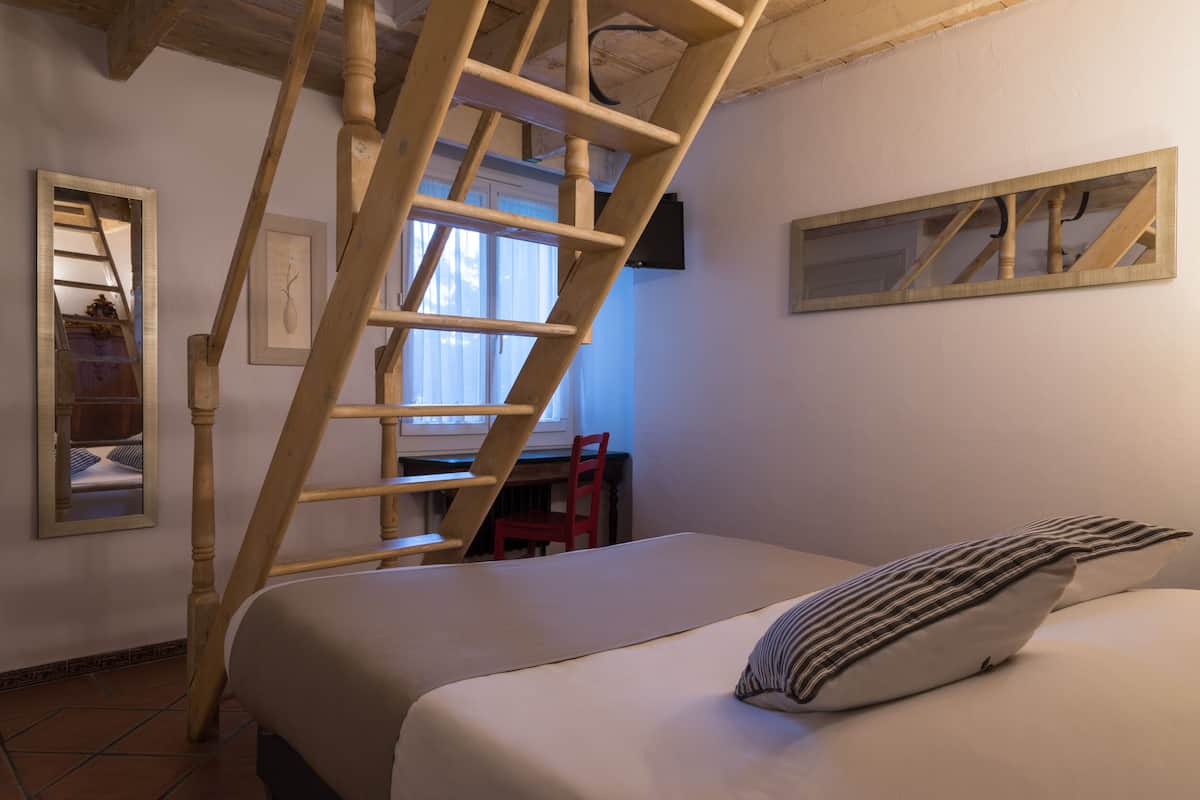 Une chambre avec une échelle en bois, un lit avec des coussins à rayures, une chaise rouge et un bureau avec une chaise.