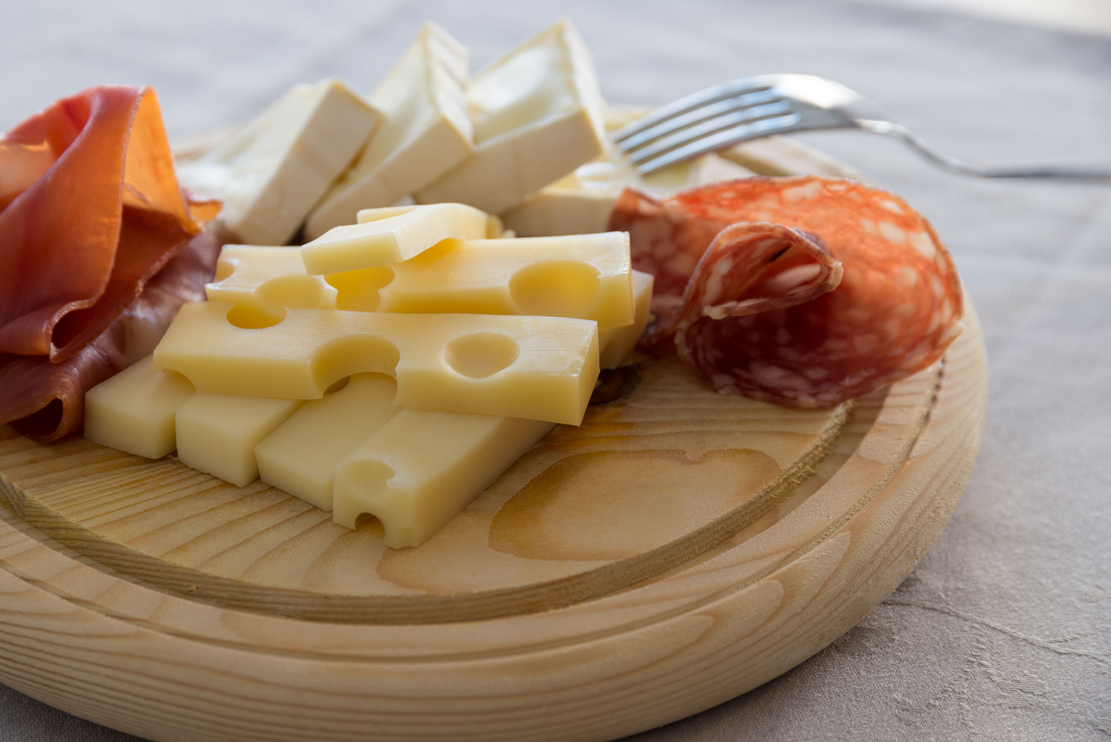 A wooden board with various cheeses and cured meats.