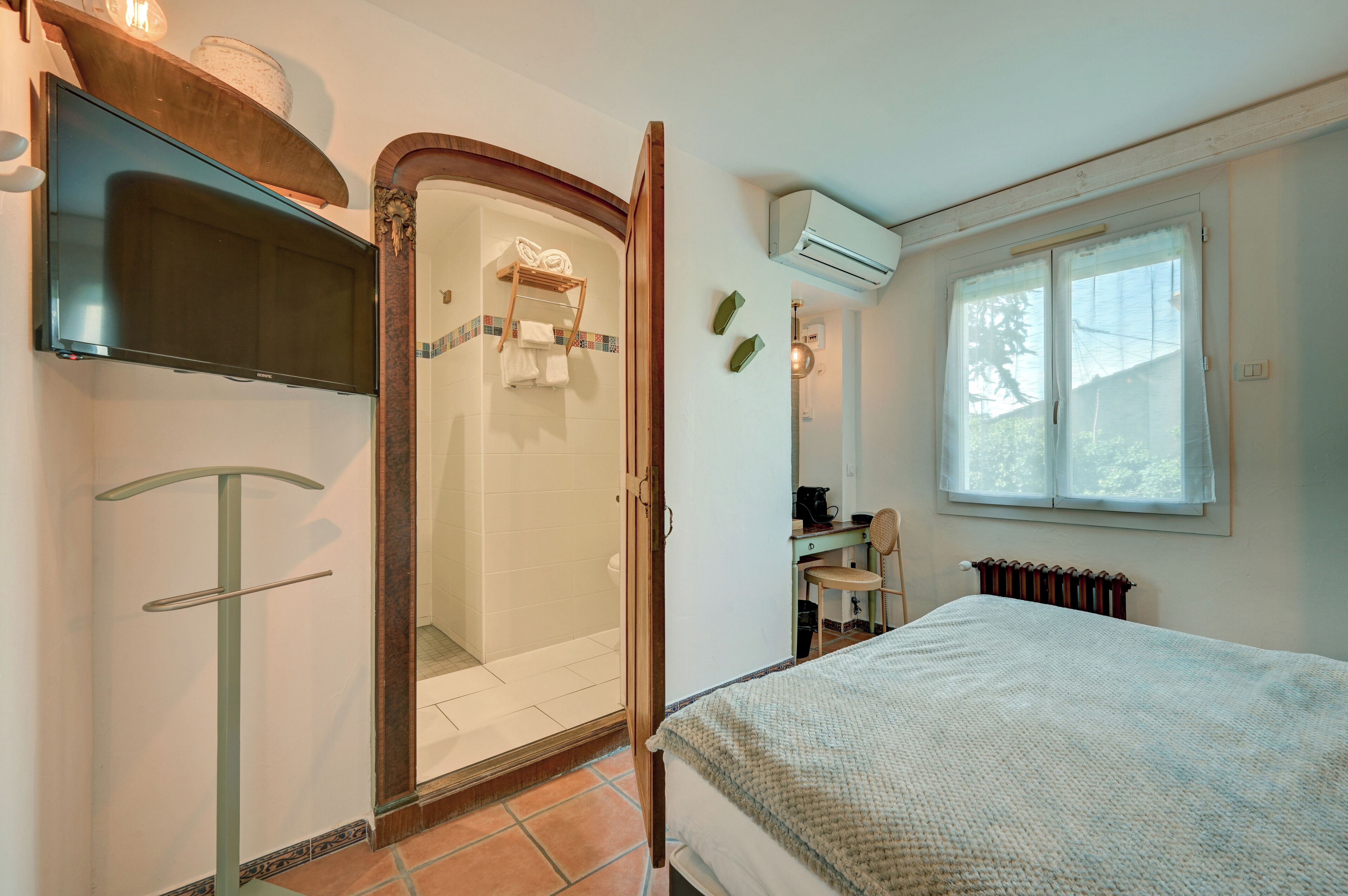 Un dormitorio con cama, televisor, ducha y ventana con cortinas.
