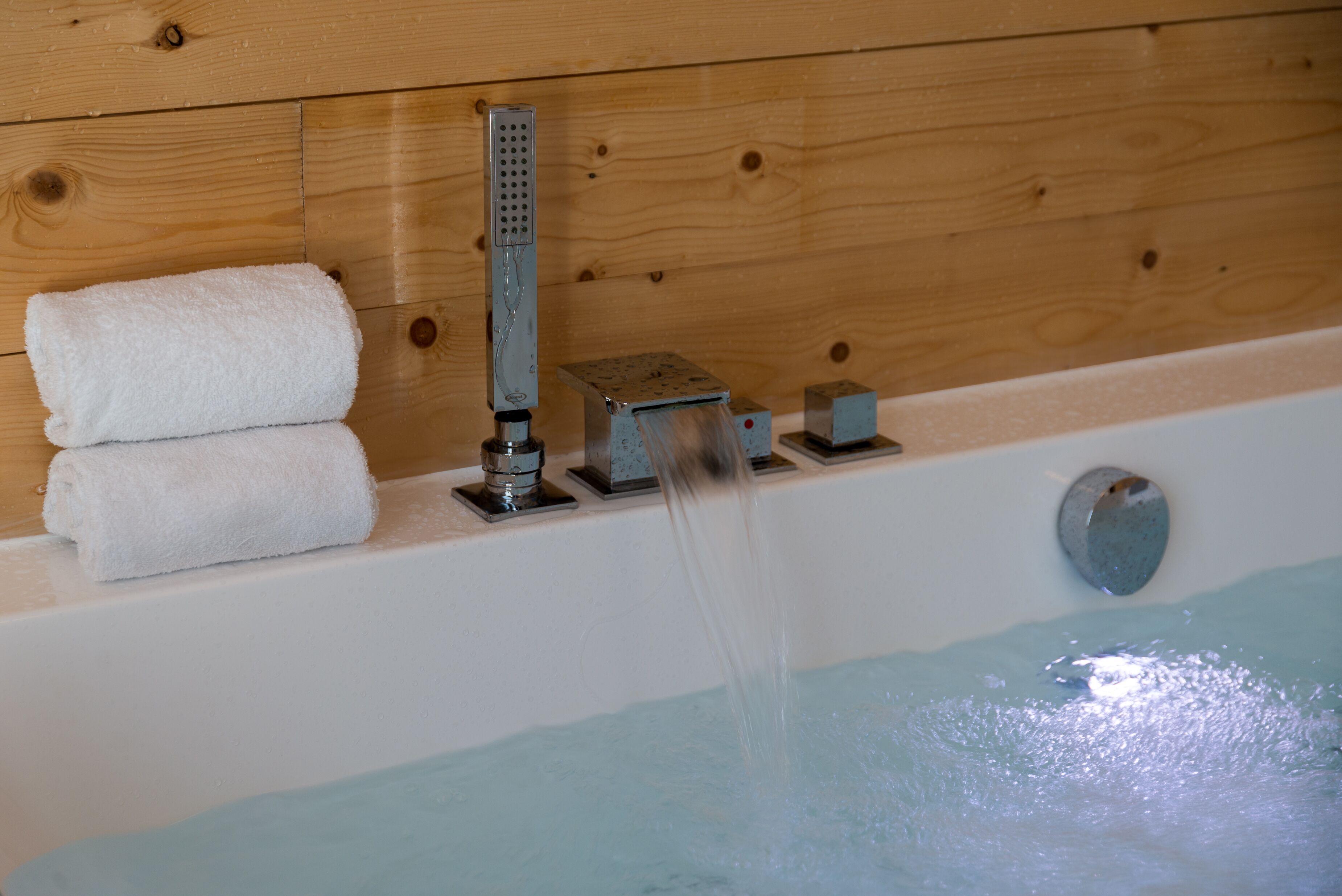 Una bañera con cabezal de ducha, una toalla y un panel de pared de madera.
